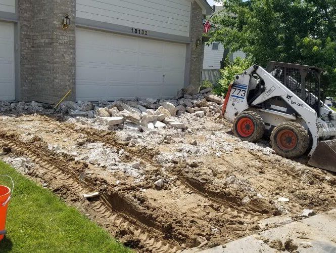 A skid steer removing an entire concrete driveway